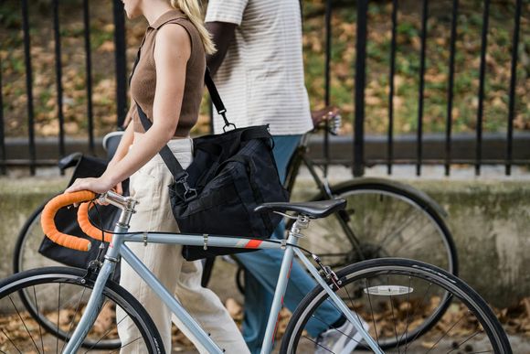 Woman walking beside a bicycle with orange handlebars and a man, near a wrought iron fence.