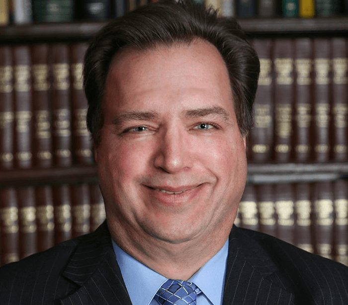 Man in suit smiling in front of a bookshelf filled with books.