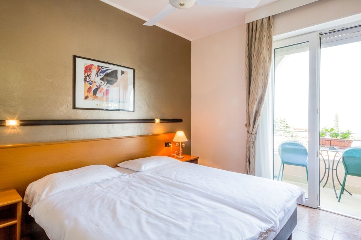 Bright hotel bedroom with two white beds, orange headboard, and balcony doors to a small patio
