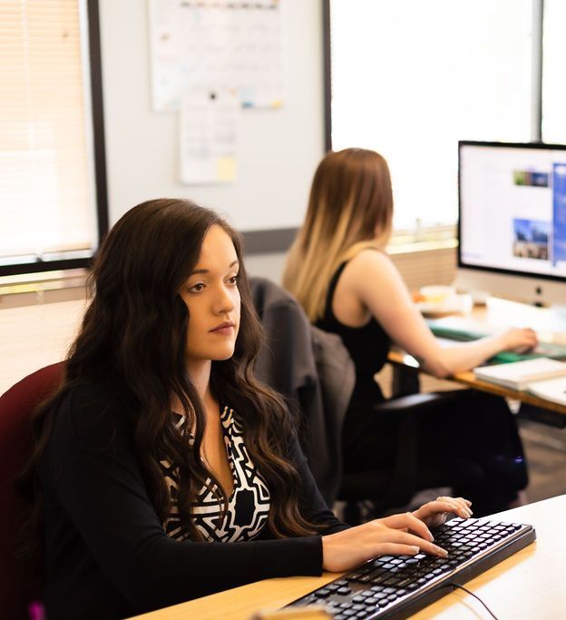 A woman is typing on a keyboard in front of a computer monitor