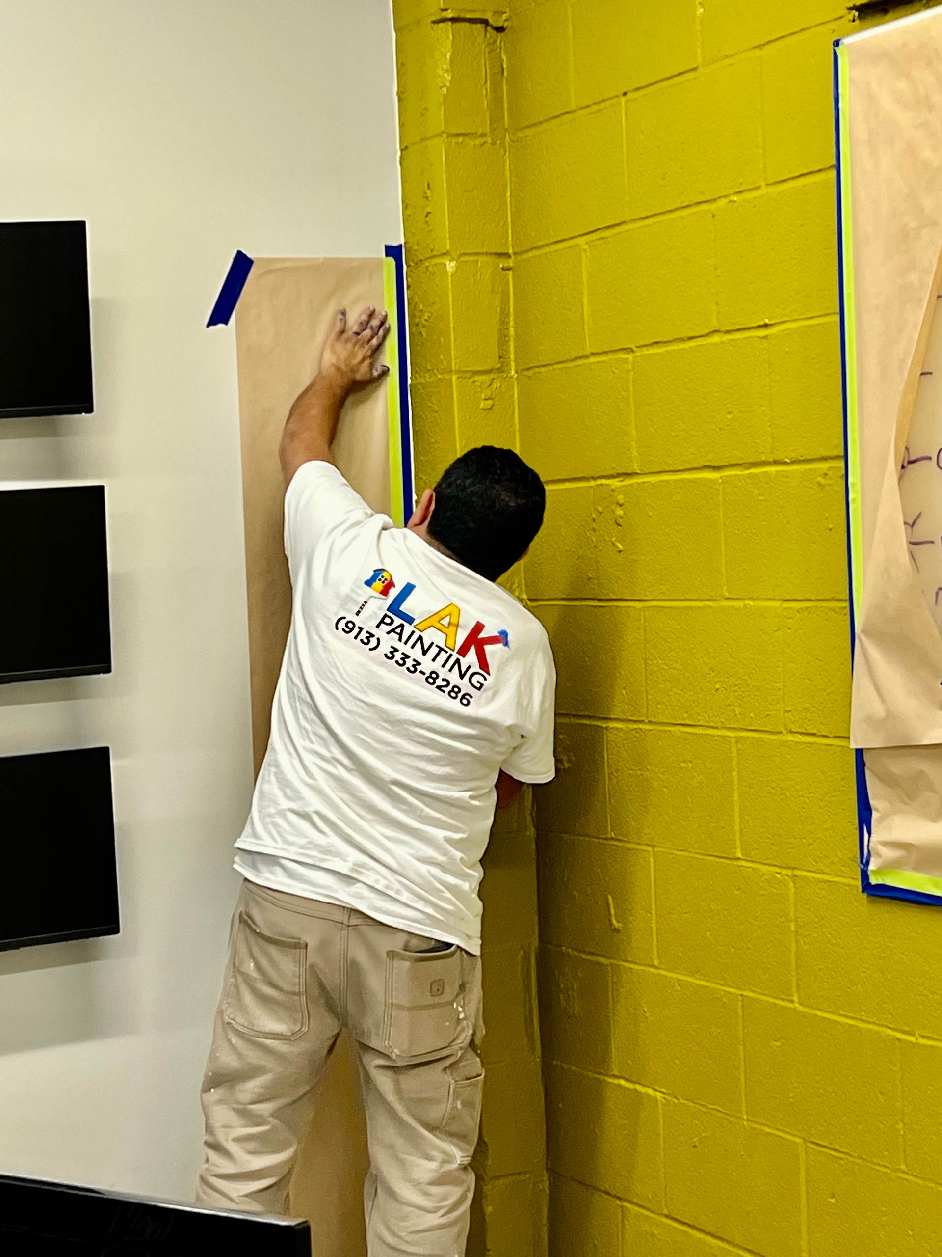 A man is painting a yellow brick wall.