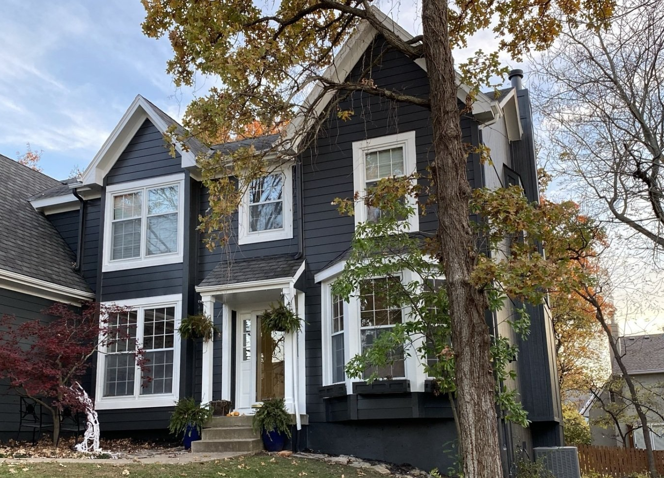 A large black and white house with a tree in front of it.