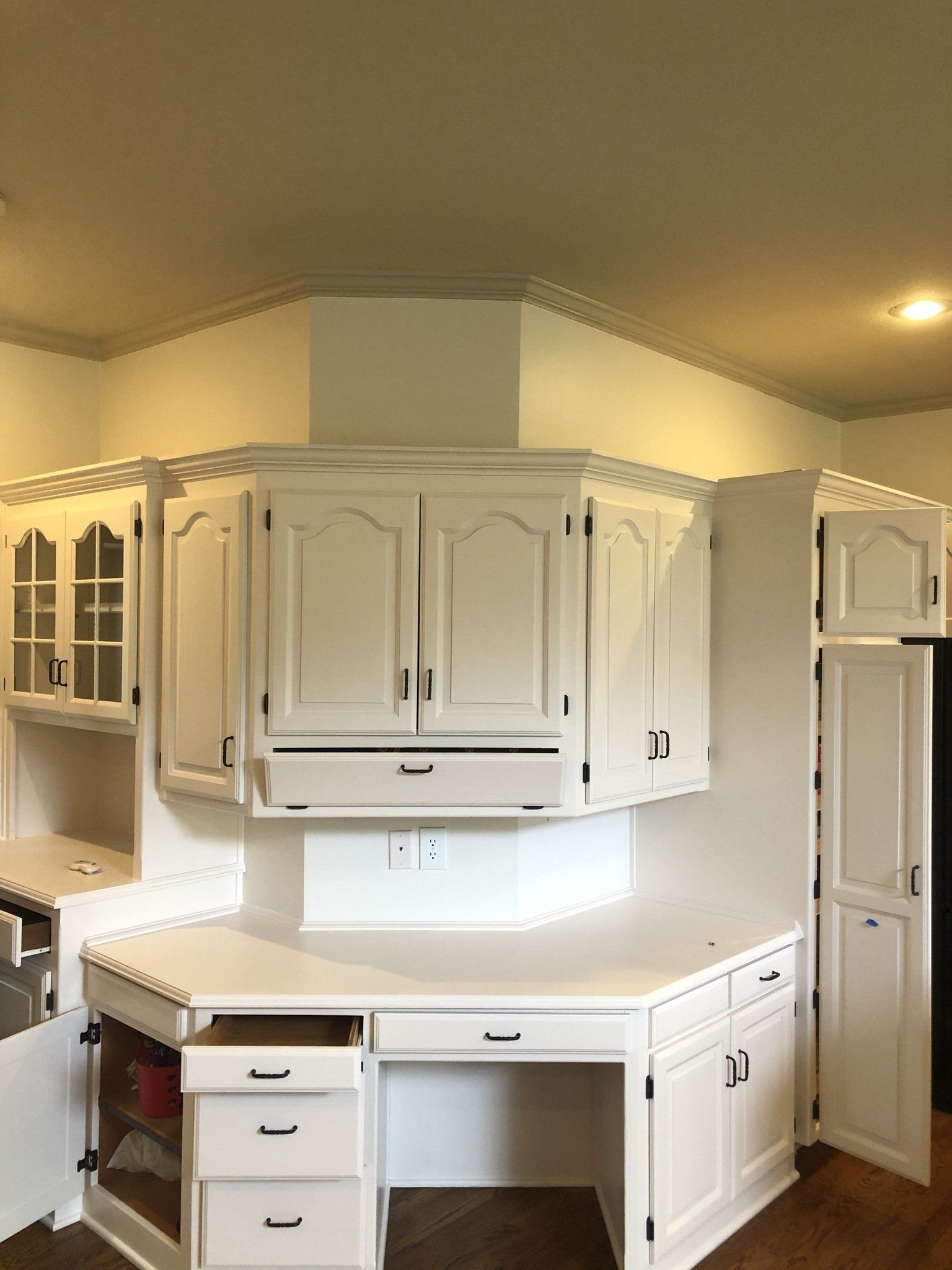 A kitchen with white cabinets and drawers and a desk