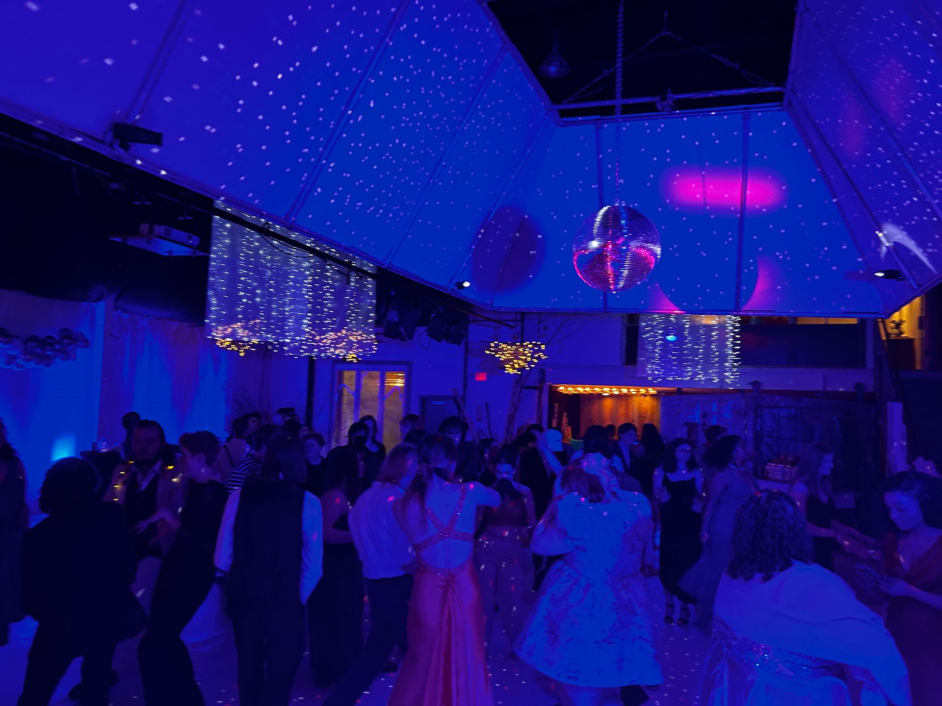 A large group of people are dancing in a room with blue lights on the ceiling.