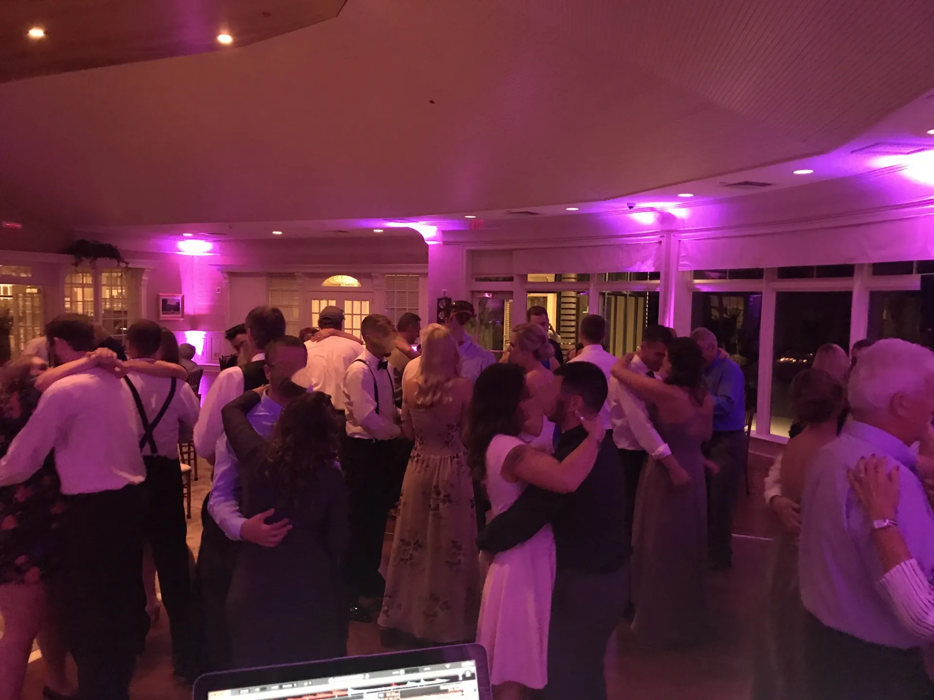 A large group of people are dancing in a room with purple lights.