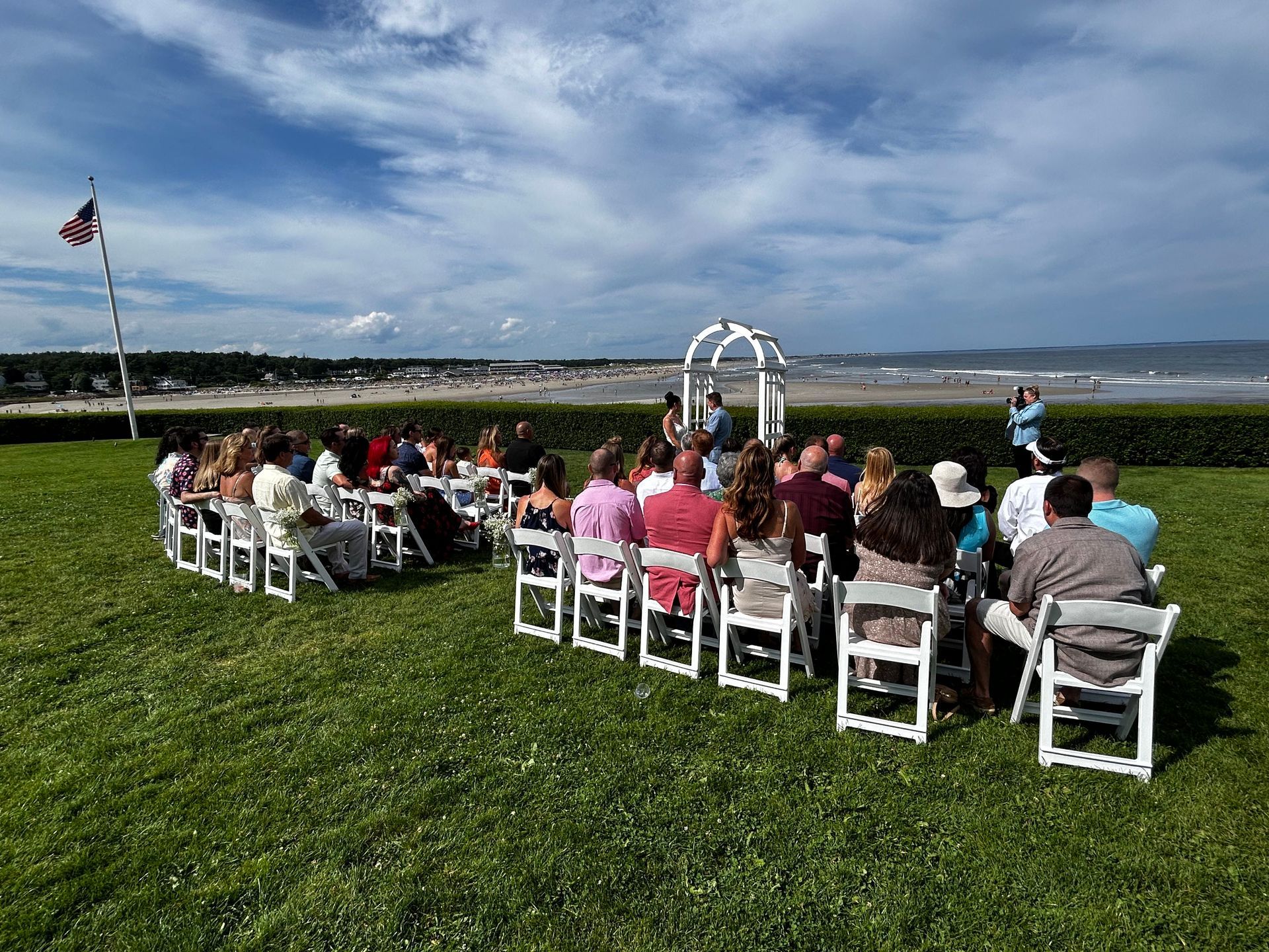 a group of people are sitting in chairs in a grassy field attending a wedding ceromony.
