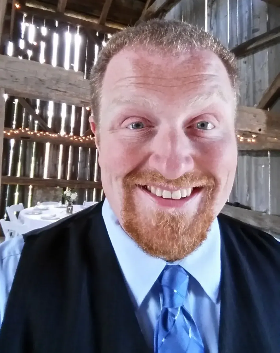 A man with a beard wearing a vest and tie smiles for the camera