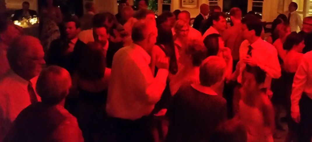 A large group of people are dancing in a dark room with red lights.