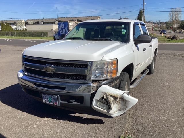 A white truck with a toilet seat on the front is parked on the side of the road.