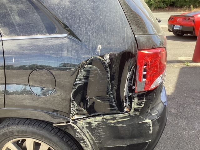 A black car with a damaged bumper is parked in a parking lot.