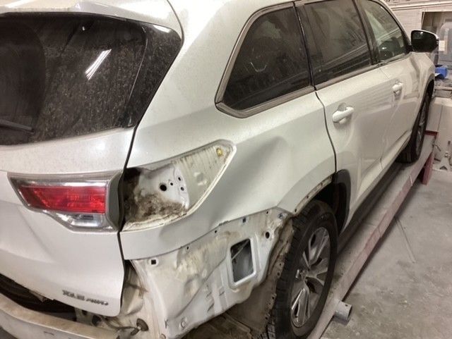 A white car with a damaged side is sitting on a lift in a garage.