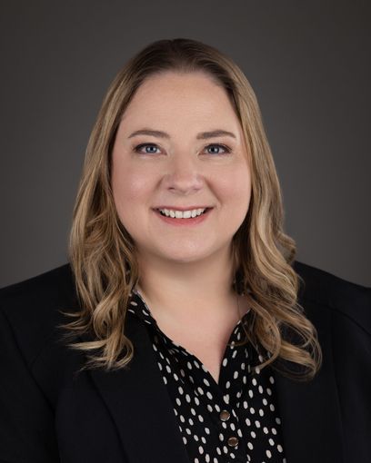 A woman in a black jacket and polka dot shirt is smiling for the camera.