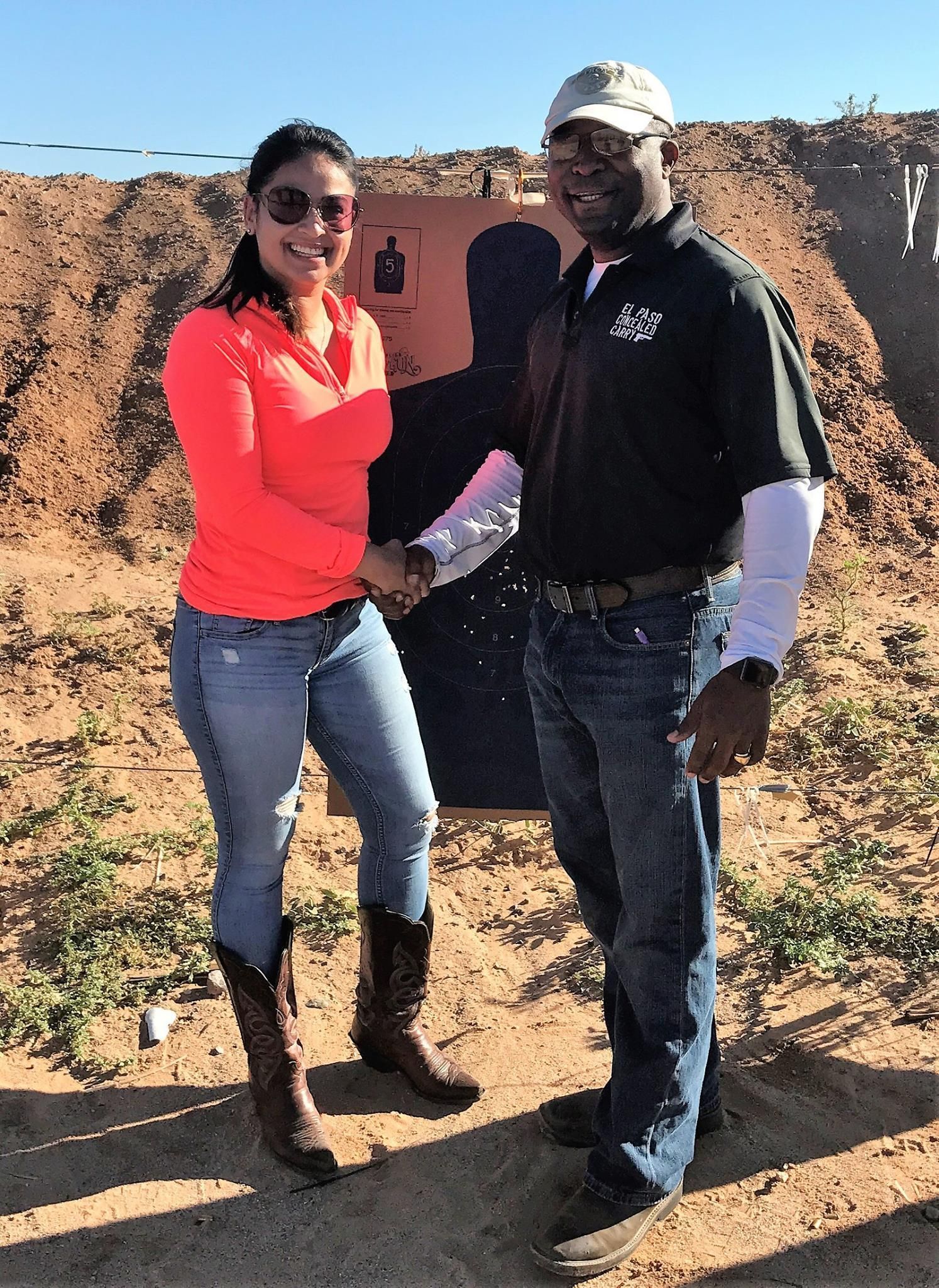 Woman and man shaking hands at an outdoor shooting range; target in the background.