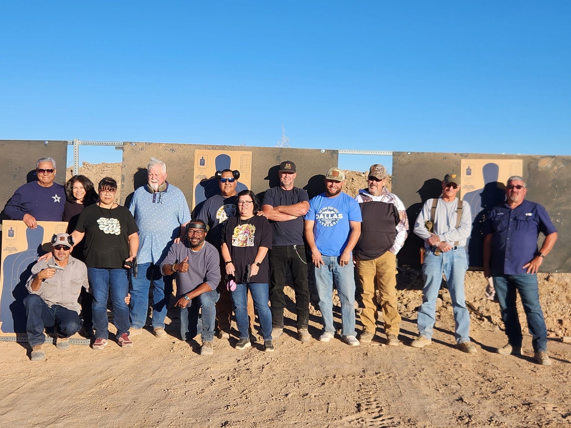 Group of people standing in front of shooting range targets, under a blue sky.