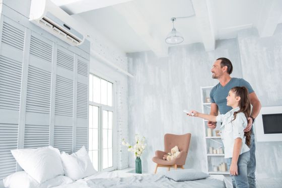 A man and a girl are adjusting the air conditioner in a bedroom.