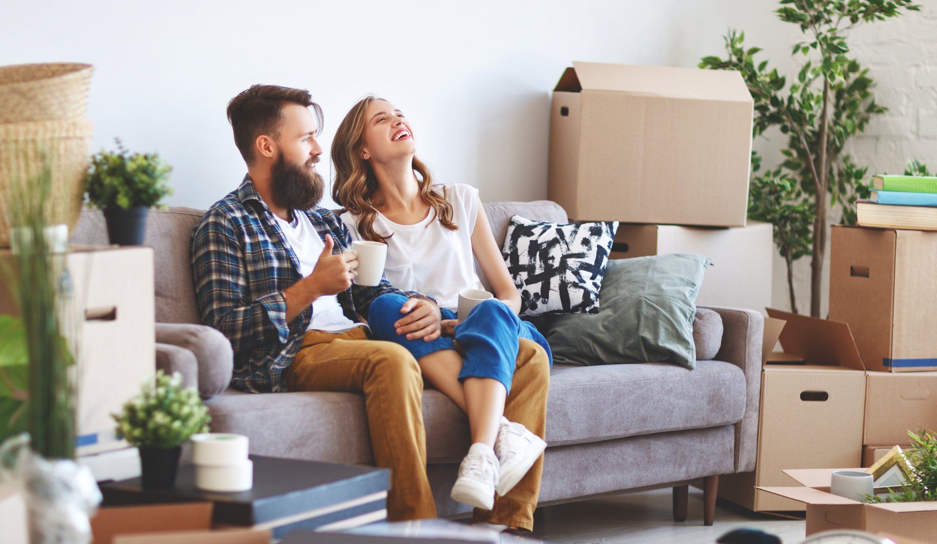 A man and a woman are sitting on a couch in a living room surrounded by cardboard boxes.