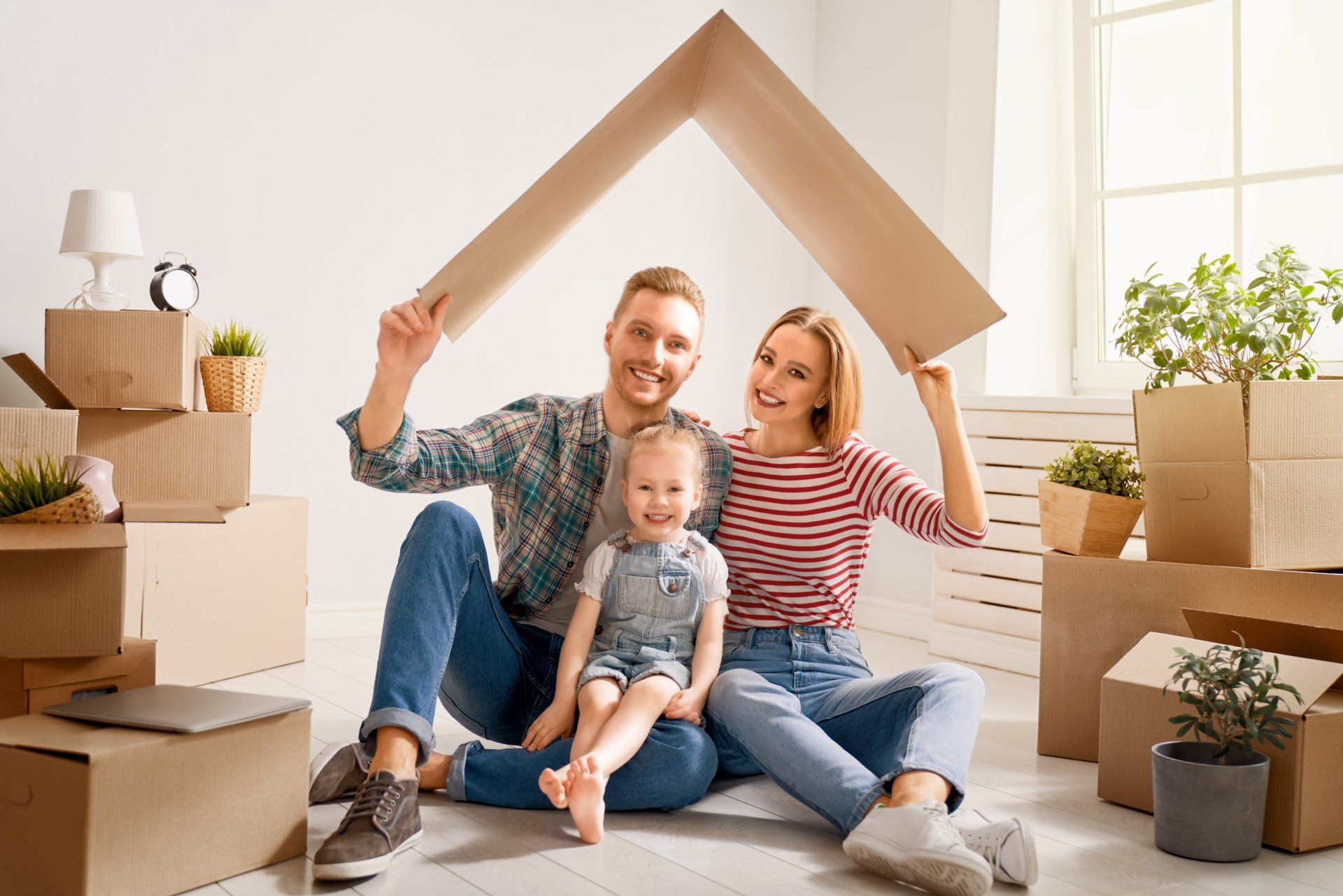 A family is sitting on the floor under a cardboard house.