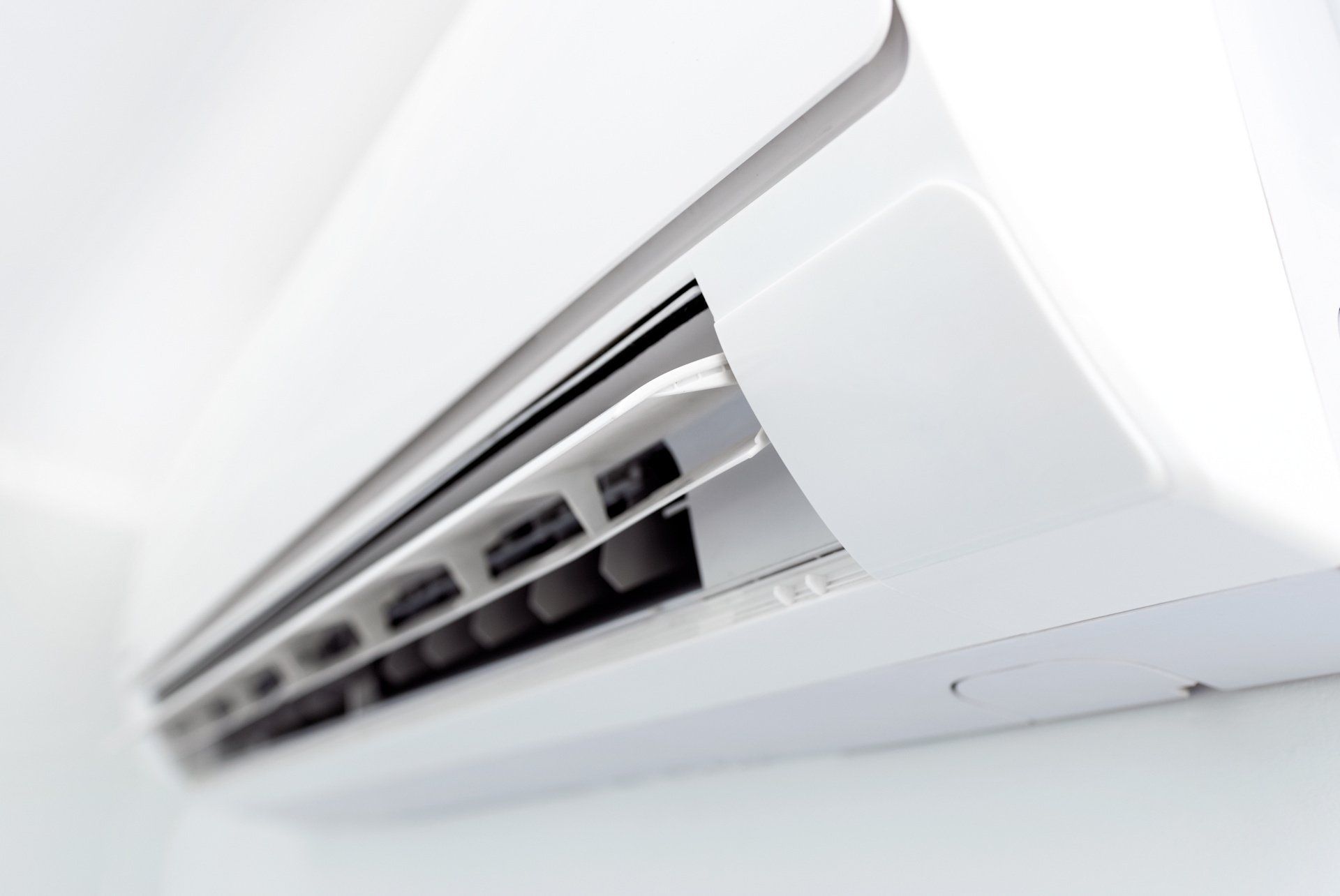 A close up of a white air conditioner on a white wall.