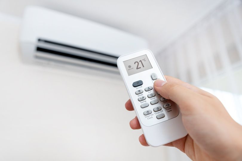 A person is holding a remote control in front of an air conditioner.