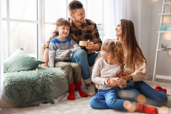 A family is sitting on the floor in front of a window drinking coffee.