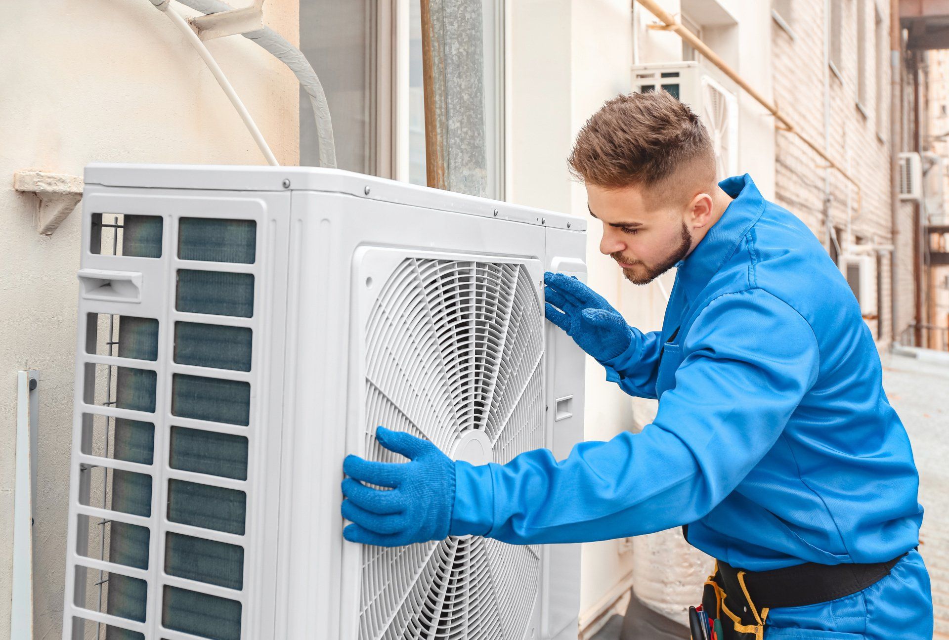 A man in a blue jacket is installing an air conditioner on the side of a building.