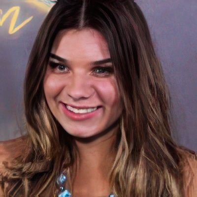 A woman with long hair is smiling and wearing a blue necklace