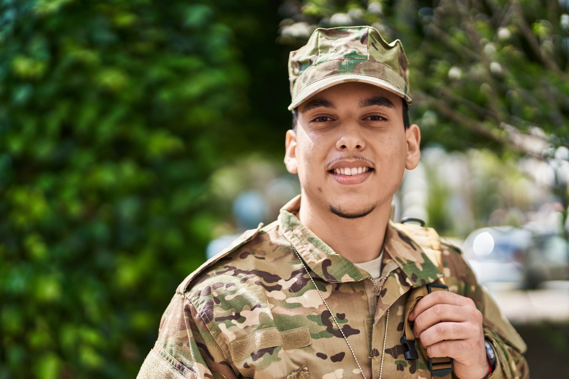 Man in camouflage uniform smiles, outdoors.