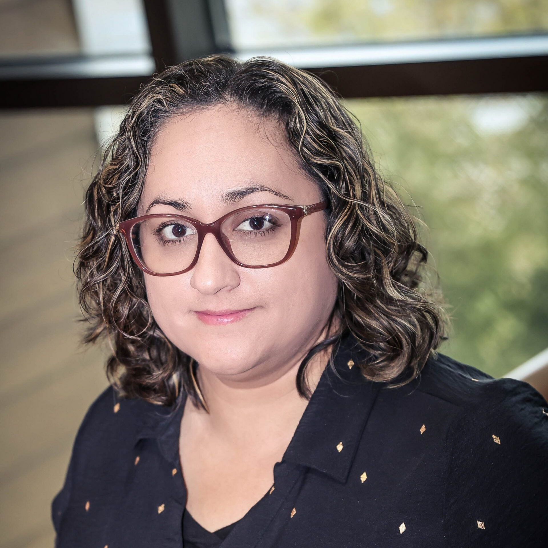 Woman with curly brown hair wearing glasses, black shirt, smiling.