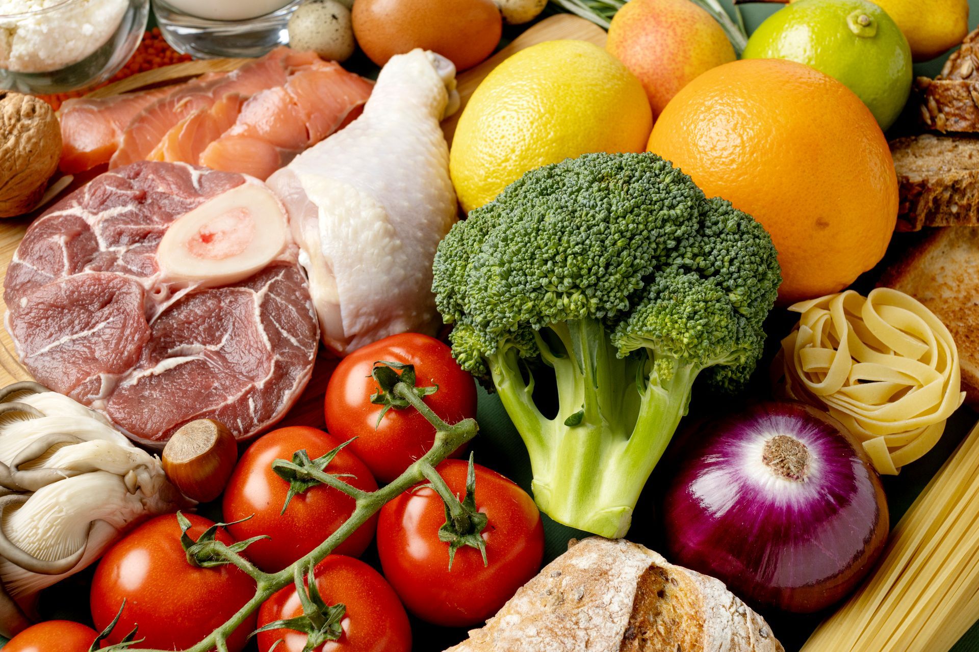 Assortment of fresh produce and protein: meat, poultry, broccoli, tomatoes, lemons, oranges, onions, eggs, and bread.