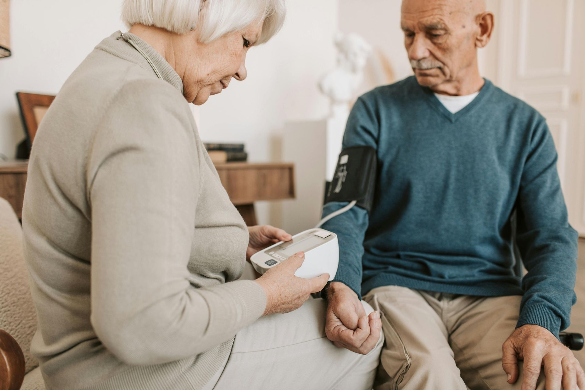 Woman taking man's blood pressure with a digital monitor in a home setting.