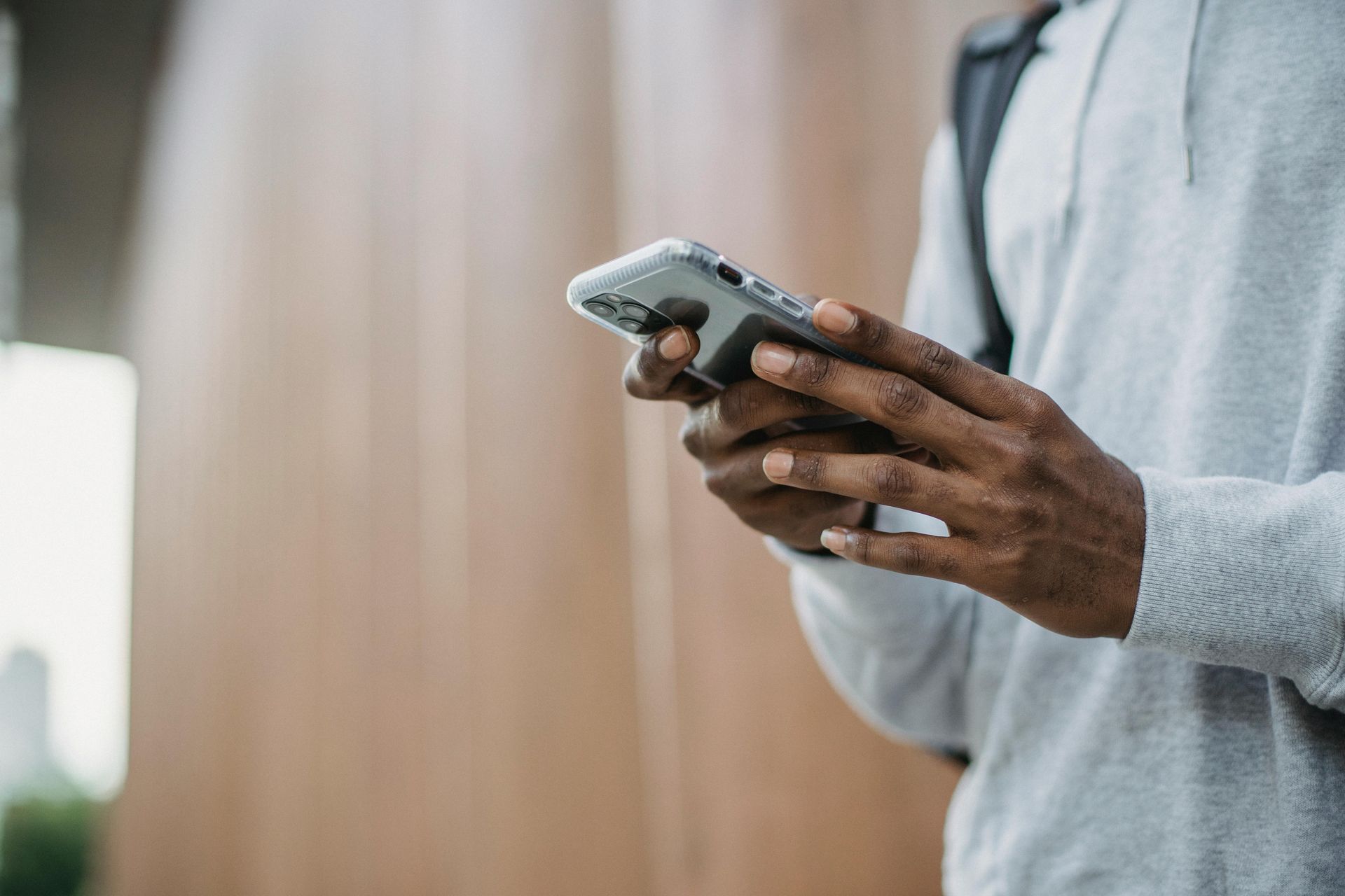 Person holding a smartphone, typing. Wearing a gray long-sleeved shirt with a backpack.White logo.