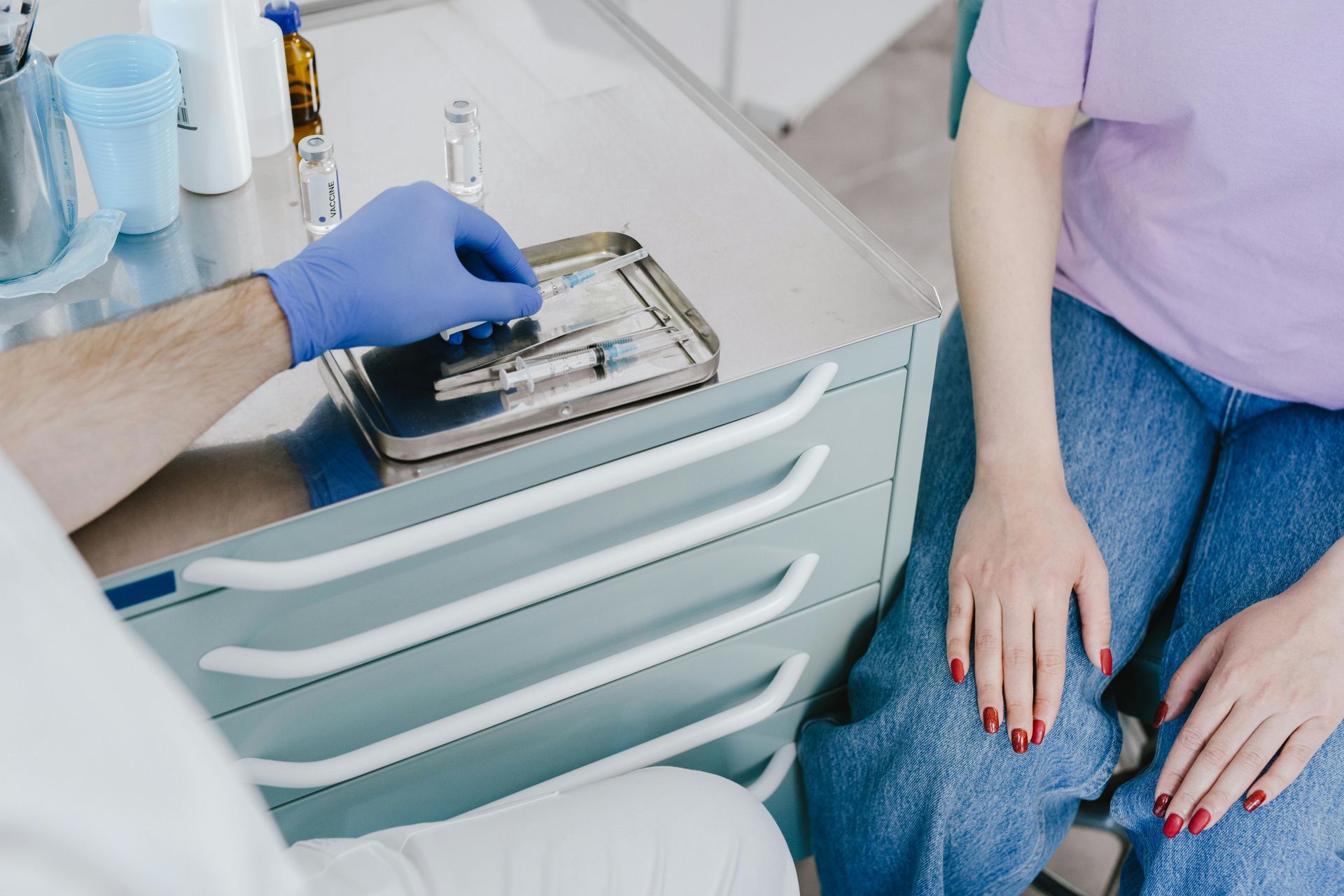 Person receiving an injection from a medical professional, preparation on a nearby tray.