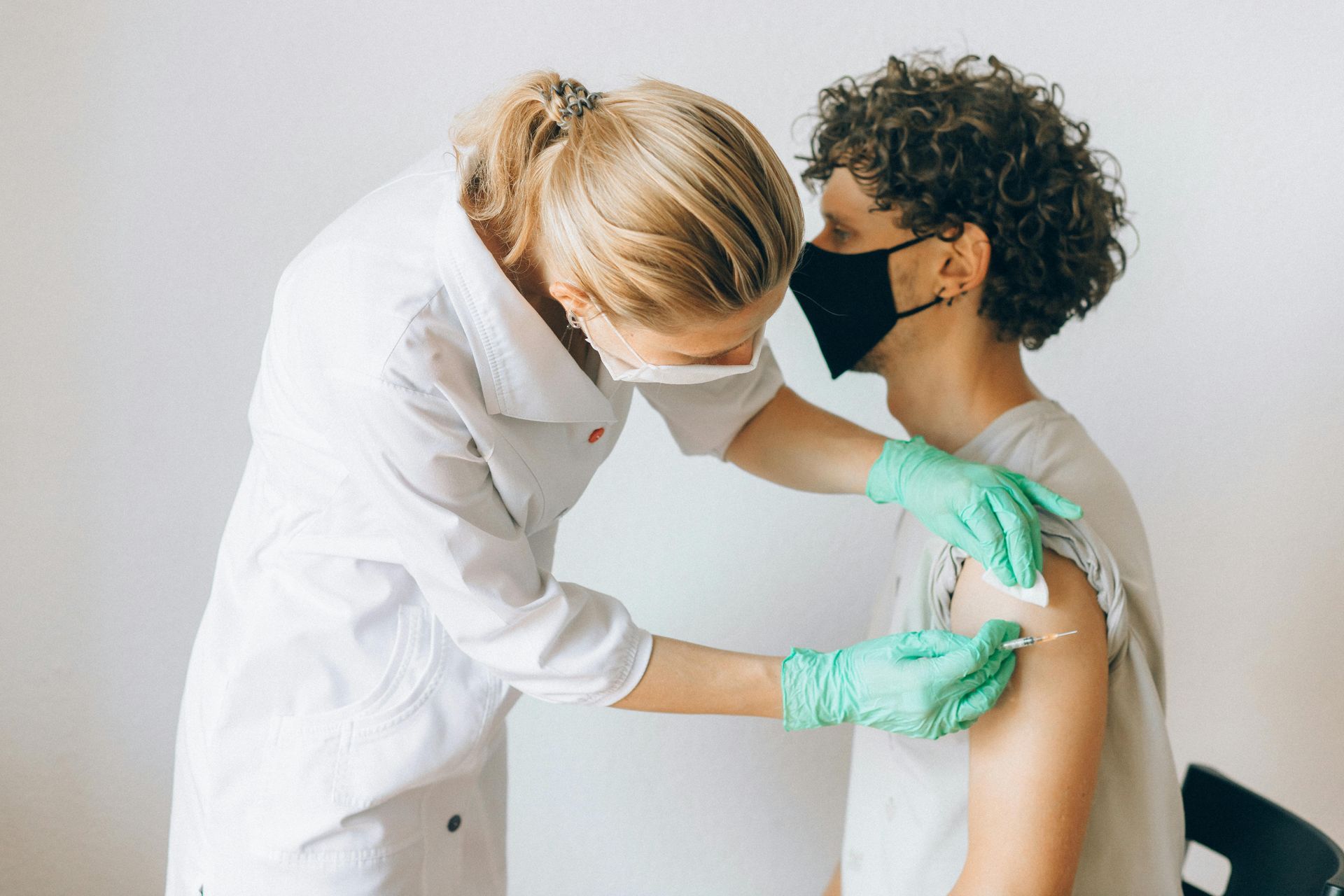 Medical professional giving a vaccine to a person wearing a mask. White coat, gloves, and medical equipment.