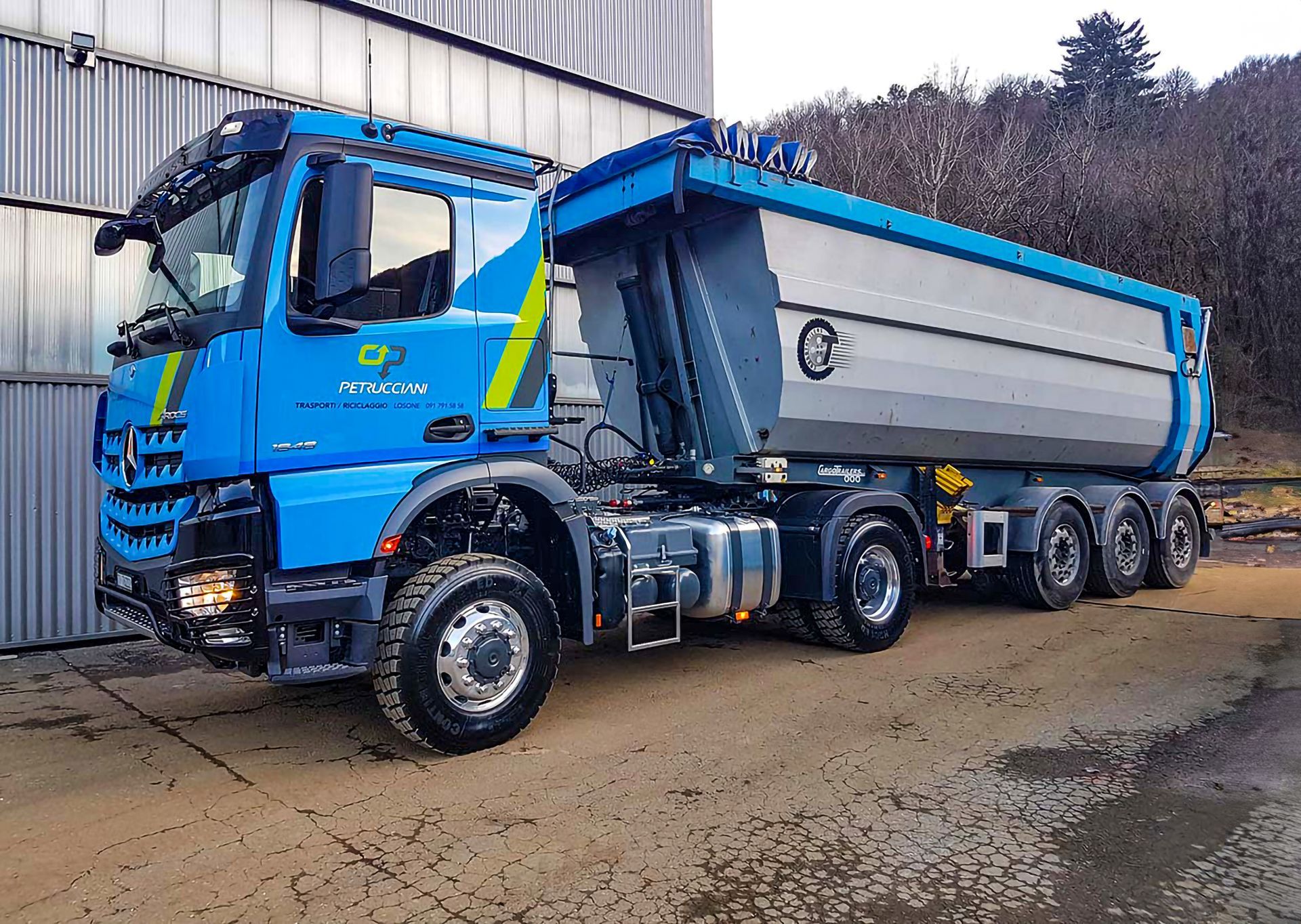 Un camion con cassone ribaltabile blu è parcheggiato davanti a un edificio.