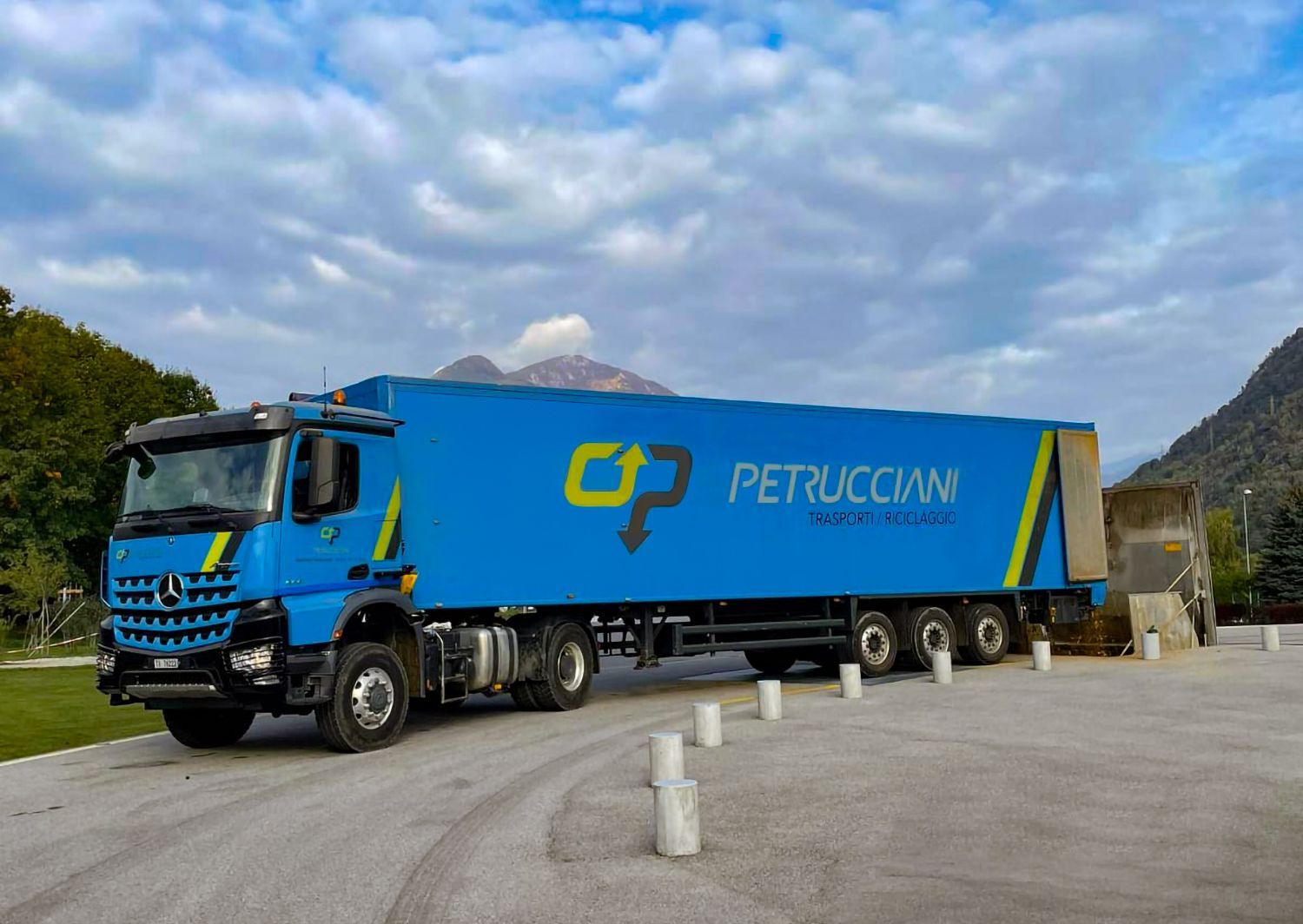 Un camion blu è parcheggiato in un parcheggio con le montagne sullo sfondo.