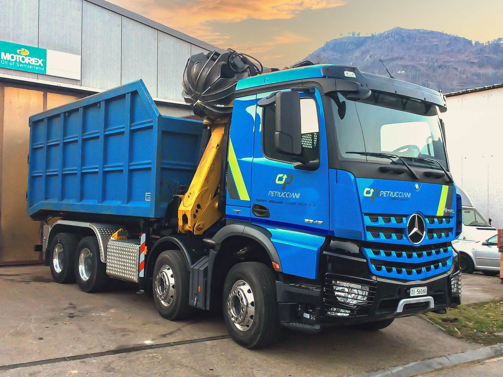 Un camion con cassone ribaltabile blu è parcheggiato davanti a un edificio.