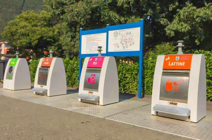 quattro contenitori per la separazione dei rifiuti davanti ad un bosco