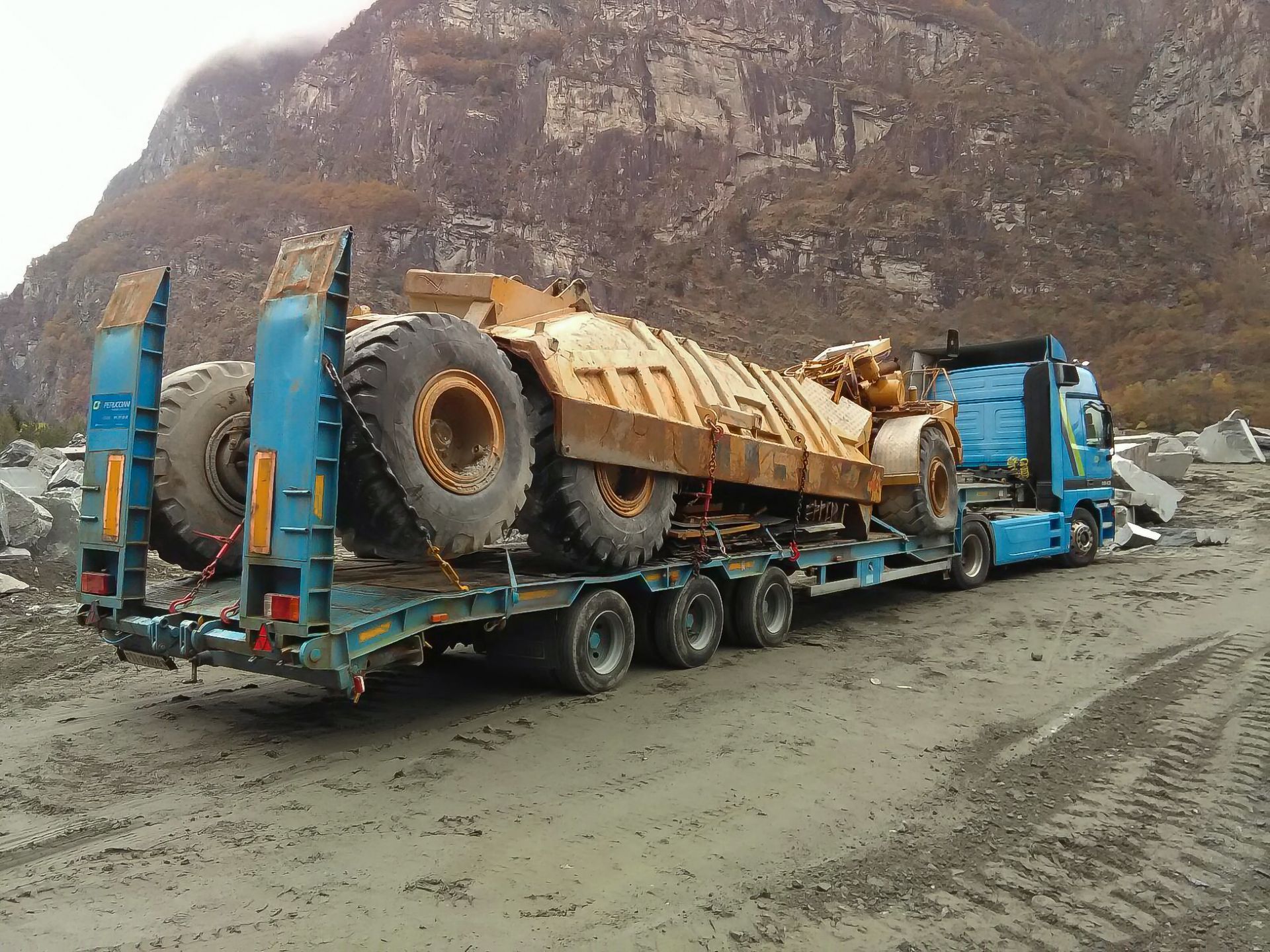 Un camion blu trasporta un grande autocarro con cassone ribaltabile giallo