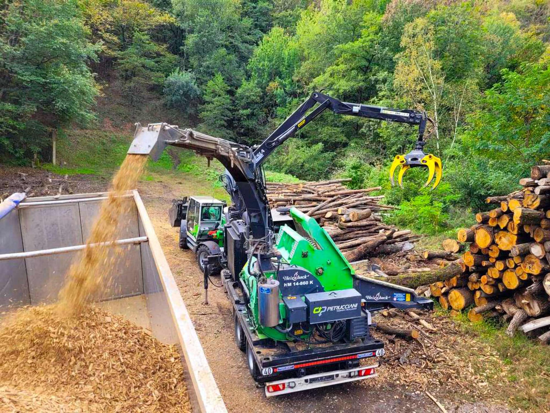 Immagine con macchinario che trita legname e lo carica su un autocarro