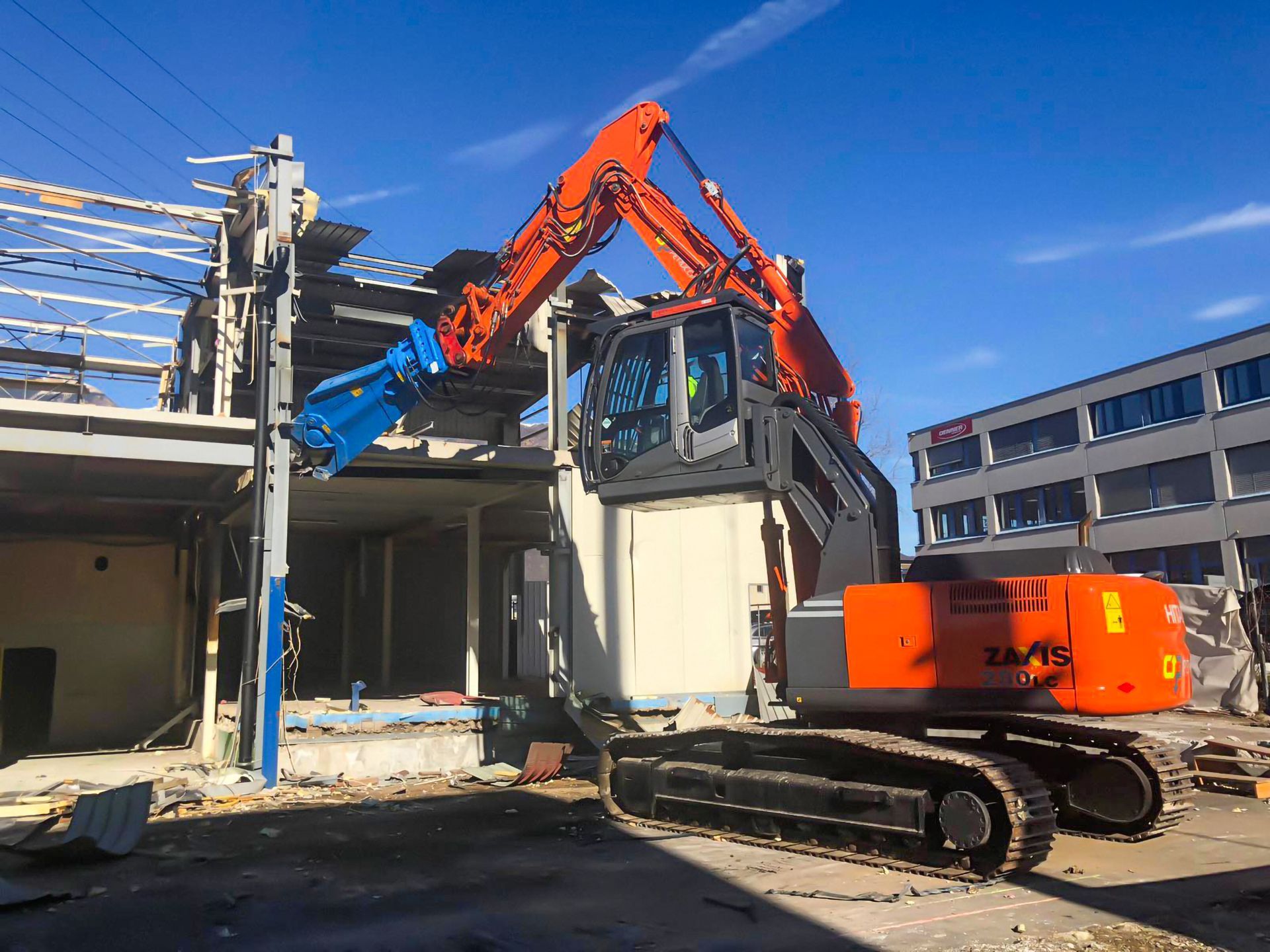 Un grande escavatore arancione sta demolendo un edificio.