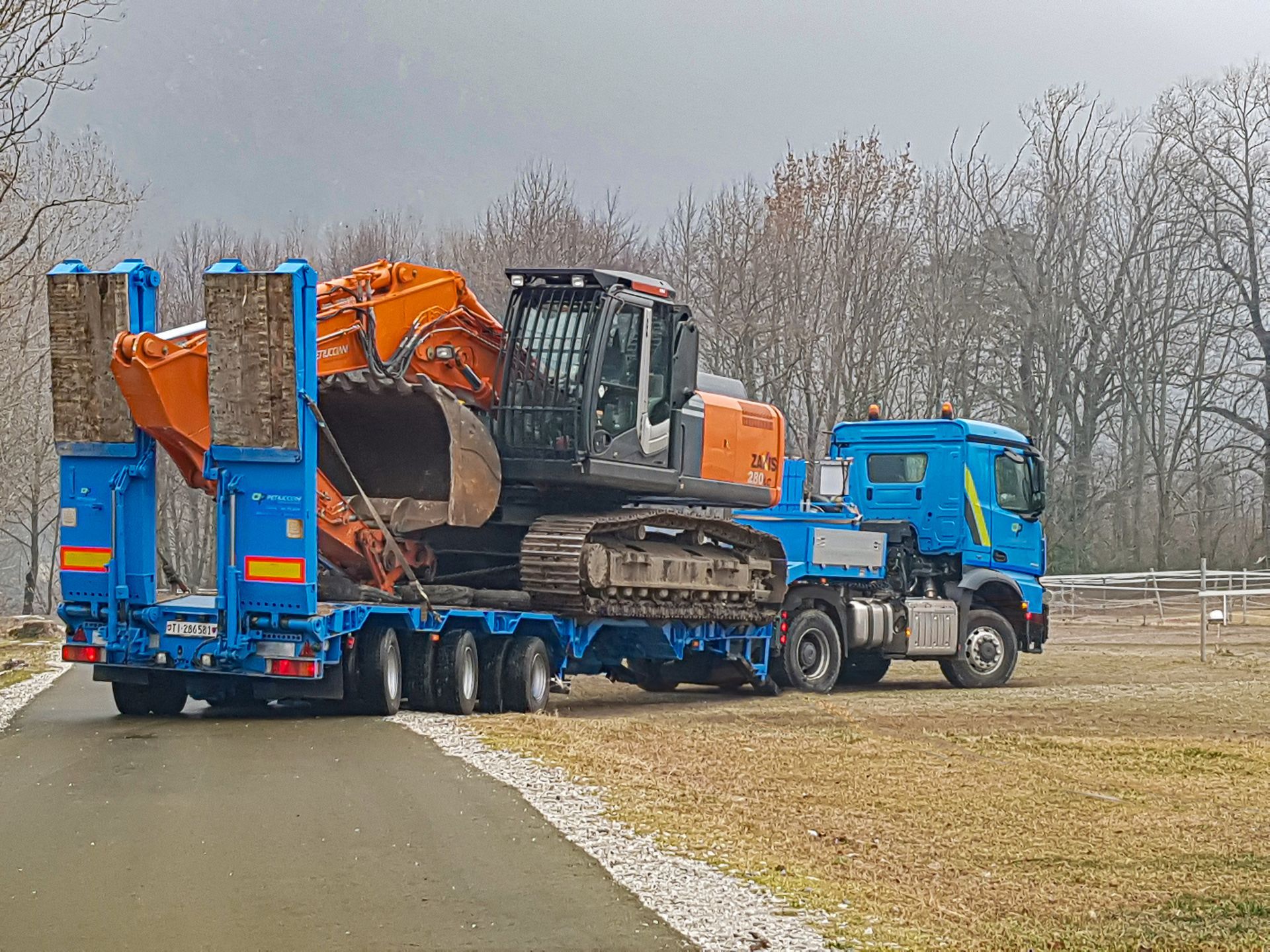 Un camion blu trasporta un grande escavatore su un rimorchio.