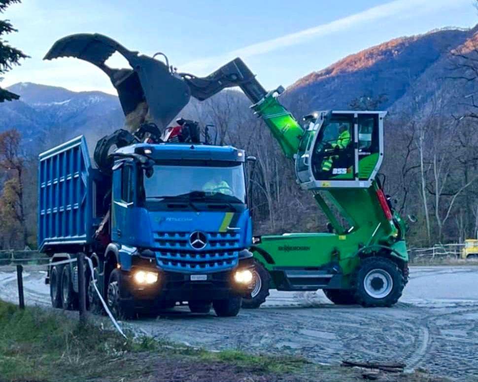 Un camion blu viene caricato con una gru verde.