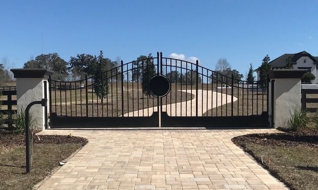 A black gate is sitting on top of a brick driveway.