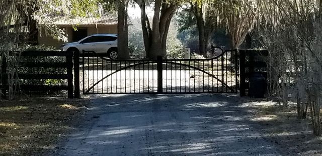 A car is parked in front of a metal gate on a dirt road.