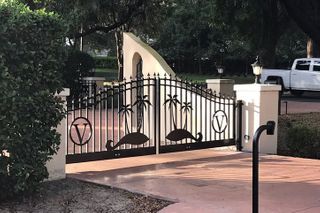 A white truck is parked in front of a wrought iron gate with flamingos on it.