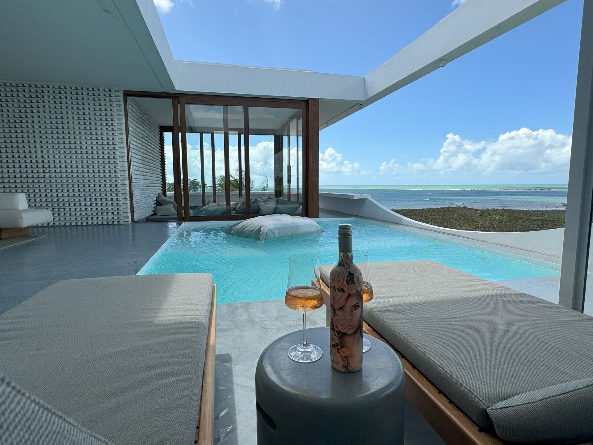 Uma garrafa de vinho está sobre uma mesa ao lado de uma piscina.