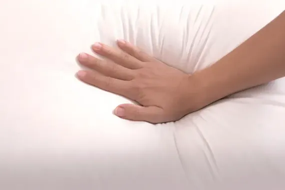 Mano presionando una almohada blanca y esponjosa.