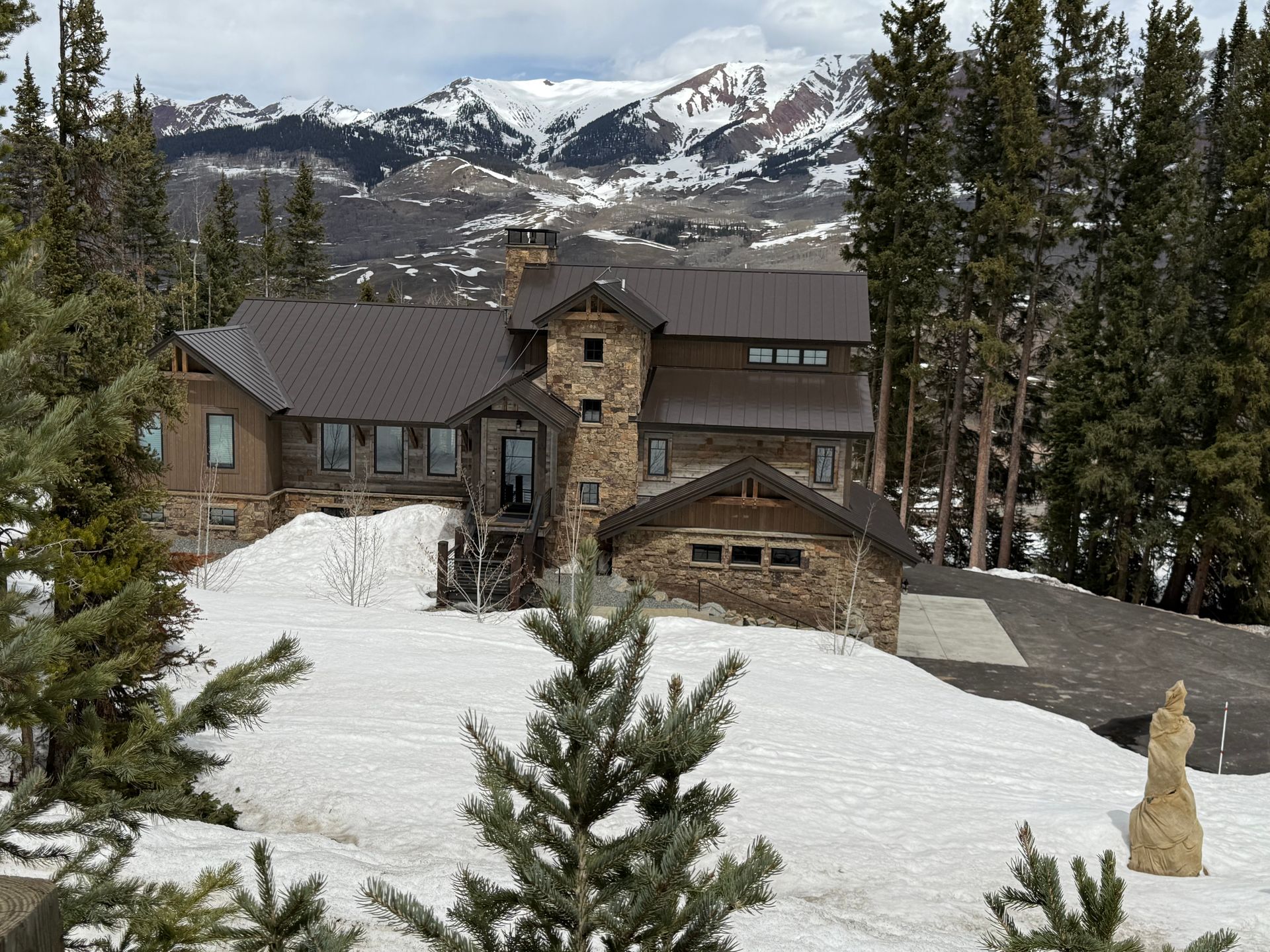 Stone house nestled in snowy landscape with mountain backdrop and evergreens.
