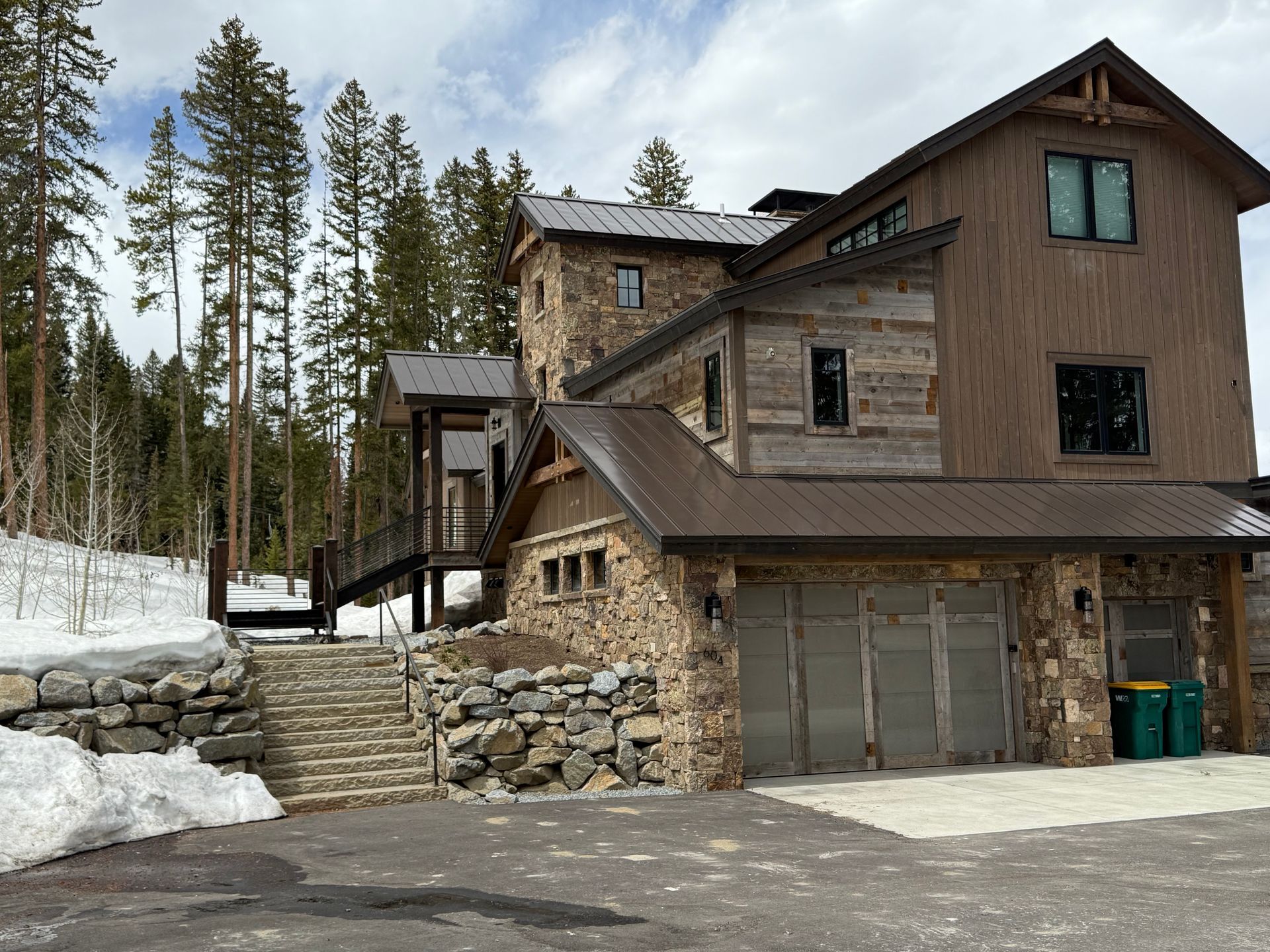 Stone and wood multi-level mountain home with a garage, stairs, and connecting bridge.
