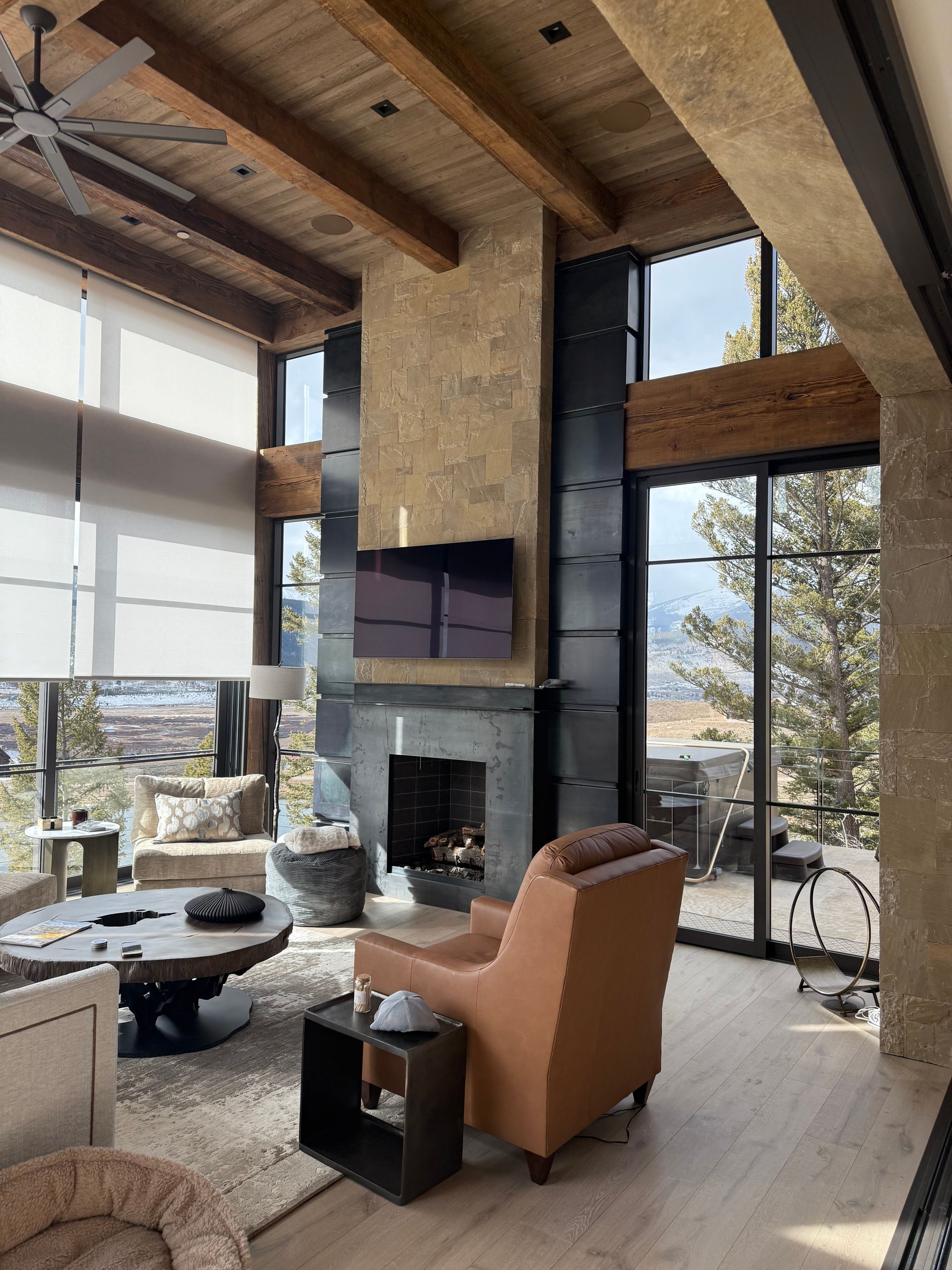 Living room with tall windows, stone fireplace, wooden beams, and an orange armchair.